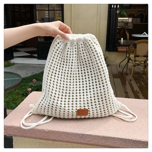 Macro detail of creamy white crochet knit backpack featuring mesh texture and leather tag