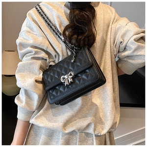 Détail d'un sac bandoulière noir matelassé avec boucle nœud en métal argenté et chaîne