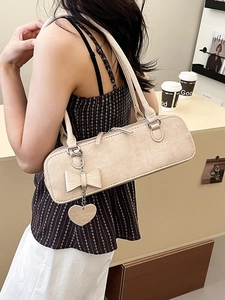 Sac sous le bras beige embossé crocodile avec nœud et pendentif cœur porté par un mannequin