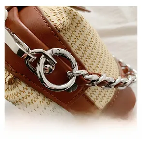 Detail of silver metal buckle and chain on beige woven texture with brown leather trim
