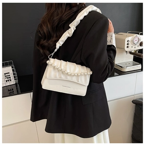Close-up of beige pleated cloud bag with pearl chain detail worn on woman's shoulder