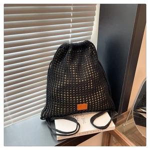 Detail of black crochet drawstring backpack with hollow mesh pattern and leather logo patch