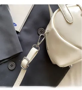 Close-up of shiny cream patent leather bag with silver hardware and adjustable strap