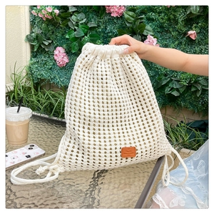 Detail of crochet knit texture and brown leather label on cream drawstring bucket bag