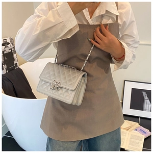 Détail du sac bandoulière argenté matelassé avec nœud métallique porté par le mannequin