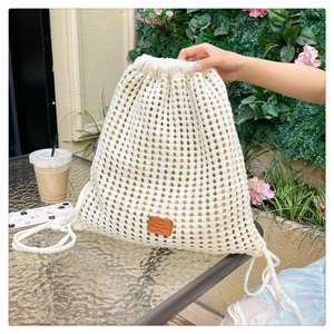 Detailed knit texture of white crochet drawstring bucket bag with a brown leather label
