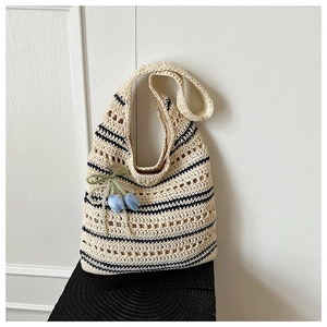 Detail of hollow woven straw bag with black stripes and a blue tulip charm pendant