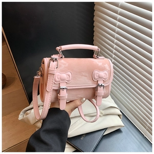 Close-up of pink cylinder handbag with bow buckles and glossy patent leather finish
