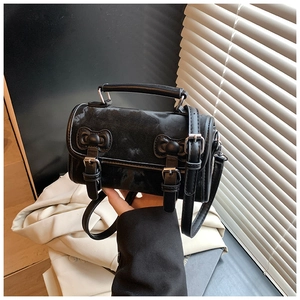 Detail view of a black cylindrical crossbody bag with vintage buckle straps and top handle