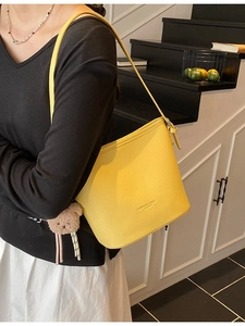 Yellow bucket bag with plush bear charm and pebbled texture for trendy casual commuting