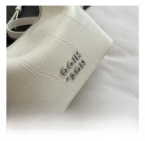 Detail shot of white crocodile-embossed leather with silver metal logo and high-end texture