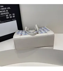 Gros plan des coutures sur cuir beige et tissu à carreaux bleus du sac cabas