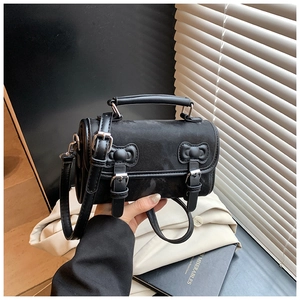Detail of black textured matte leather cylinder bag with bow and buckle accents