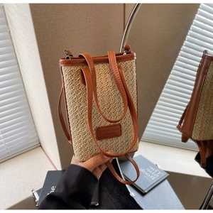 Detail of woven straw bucket bag with brown leather trim and embossed brand tag