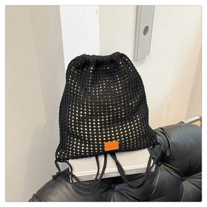 Close-up of black knitted bucket backpack featuring hollow mesh texture and orange leather label