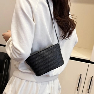 Detail of black woven leather crossbody bag worn over a white outfit for daily style
