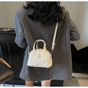 Close-up of white heart-shaped Boston bag in glossy patent leather with adjustable strap