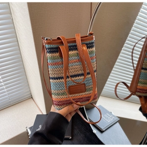 Detail of colorful woven straw bucket bag with brown leather straps and logo patch