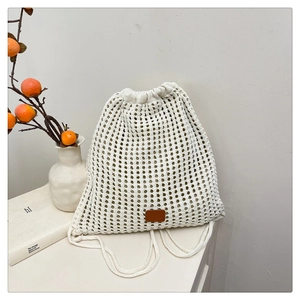 Detail of white knit drawstring backpack featuring hollow floral patterns and brown leather patch