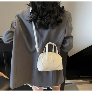 Detailed view of a white heart-shaped crossbody bag on a model wearing a grey blazer