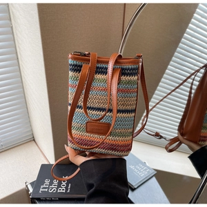 Détail du tissage rayé coloré et de la bandoulière en cuir marron d'un petit sac seau