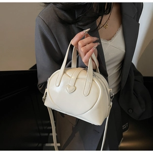 Detail of a creamy white heart-shaped boston bag held by a model in a stylish outfit