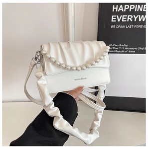Close-up of white ruched handbag with pearl chain decoration and wide scrunchie strap