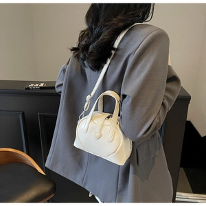 Detailed view of a white heart-shaped leather crossbody bag worn on a grey suit jacket