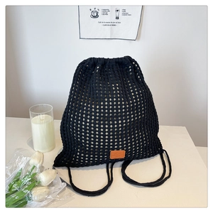 Detail of black crochet drawstring backpack featuring a woven texture and brown leather patch