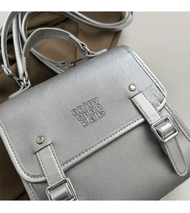 Detail of silver metallic textured crossbody bag with flap cover and vertical buckle straps