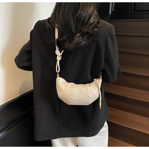 Beige high-gloss dumpling bag with knotted strap shown on model in minimalist interior