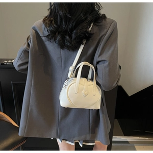 Detailed view of a white heart-shaped mini crossbody bag worn with a casual gray suit