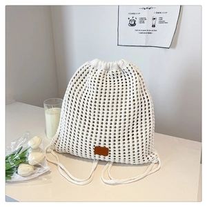 Detail of white knit drawstring backpack with bohemian cutout pattern and leather logo