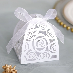 Close-up of laser-cut white wedding favor box with floral patterns and a large organza bow