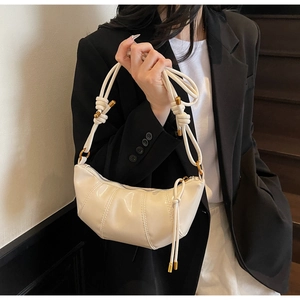 Close-up of cream crescent bag featuring thick rope knot strap and gold metal hardware