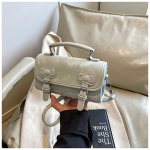 Detail of light blue PU leather handbag featuring decorative bow buckles and silver metal hardware