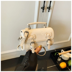 Detail of a creamy white bucket bag featuring elegant double bow buckles and round top handle