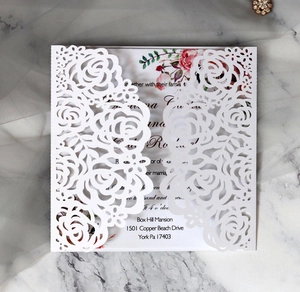 Detailed laser-cut ivory rose wedding invitation with floral insert on marble background