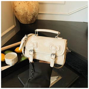 Detail of cream white leather satchel showing decorative bows and silver metal buckles