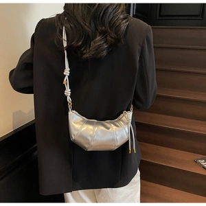 Detail of silver metallic croissant bag with knotted strap and gold hardware accents