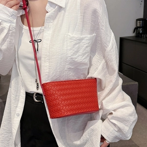 Detail of red woven leather crossbody bag showing intricate Intrecciato craft on a model