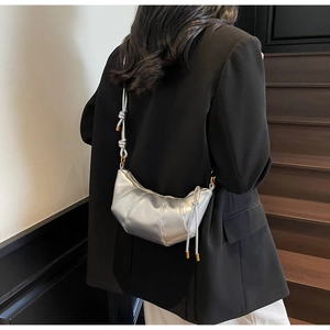 Model wearing silver metallic croissant bag with knotted strap and vertical stitching details
