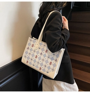 Détail des motifs brodés d'ours et de nœud sur un sac cabas en tissu texturé