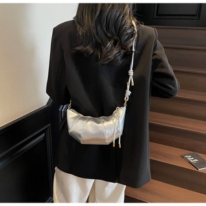 Detail of silver croissant bag with knotted strap worn by a model on stairs