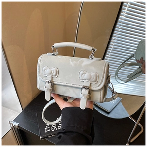 Detail of light gray square bag featuring decorative bows and twin pin-buckle straps