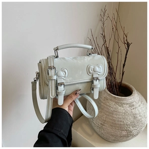 Detail of light blue crossbody bag with bow accents and adjustable strap in hand