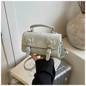 Detail of light blue crossbody bag with bow buckle decoration on a grey suitcase
