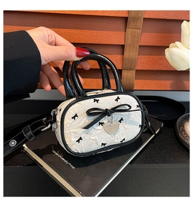 Dettaglio mini borsa a pieghe crema con pois a fiocco neri e ciondolo a cuore in metallo