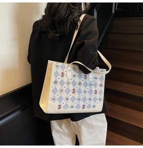 Détail d'un sac cabas beige avec des motifs bleus porté sur un escalier en bois rétro
