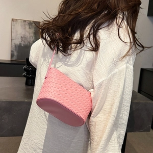 Detail of a pink woven handbag with leather straps worn by a model in a minimalist setting